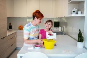 una niñita divertida que juega con masa en las manos aprendiendo a amasar ayuda a la madre adulta en la cocina, la feliz y linda hija y la madre se divierten cocinando galletas. foto