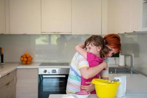 Funny little girl helper playing with dough on his hands learning to knead helps adult mom in the kitchen, happy cute baby daughter and parent mom have fun cooking cookies. photo