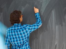 Smart Arab Teen Boy with chalk in hand writing on empty black board in school photo