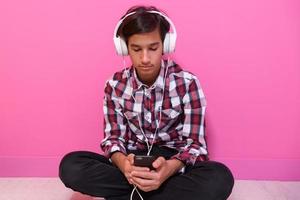 Arabic Teenage Boy Wearing Headphones And Listening To Music pink background photo