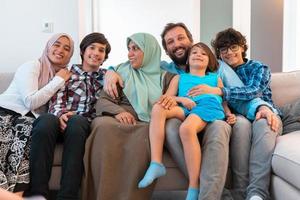 Portrait photo of an arab muslim family sitting on a couch in the living room of a large modern house. Selective focus