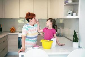 una niñita divertida que juega con masa en las manos aprendiendo a amasar ayuda a la madre adulta en la cocina, la feliz y linda hija y la madre se divierten cocinando galletas. foto