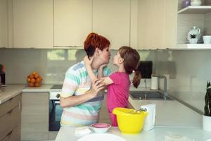 Funny little girl helper playing with dough on his hands learning to knead helps adult mom in the kitchen, happy cute baby daughter and parent mom have fun cooking cookies. photo