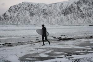 surfista ártico yendo por la playa después de surfear foto