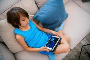 an arab boy sits on the couch and uses a tablet for fun photo