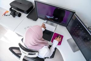 Female Arabic creative professional working at home office on desktop computer with dual screen monitor top view. Selectve focus photo