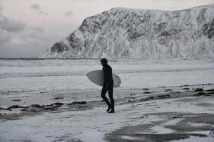 surfista ártico yendo por la playa después de surfear foto