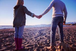 couple with dog having fun on beach on autmun day photo