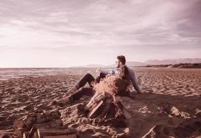 Young Couple Sitting On The Beach beside Campfire drinking beer photo