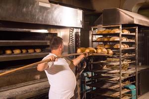 trabajador de panadería sacando panes recién horneados foto