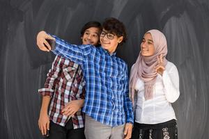 grupo de adolescentes árabes tomando una foto selfie en un teléfono inteligente con pizarra negra en el fondo. enfoque selectivo