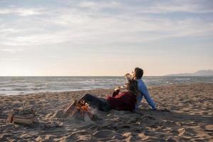 Young Couple Sitting On The Beach beside Campfire drinking beer photo