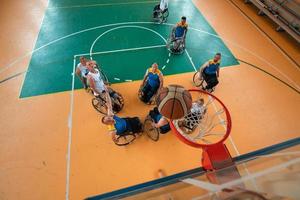 veteranos de guerra o de trabajo discapacitados equipos mixtos de baloncesto de raza y edad en sillas de ruedas jugando un partido de entrenamiento en un gimnasio deportivo. concepto de rehabilitación e inclusión de personas con discapacidad. foto