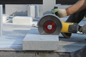 Hands of worker with electric grinder trims paving slabs on the construction site. Concept of laying new sidewalk tile. Stone cutting equipment. Road works. Civil engineering. Repair asphalt. Close-up photo