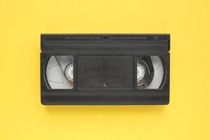 Black VHS videotape recorder cassette on yellow background. Old obsolete technology for tape recording and watching media movies. Retro, vintage, history, nostalgia concept. Top view, flat lay photo
