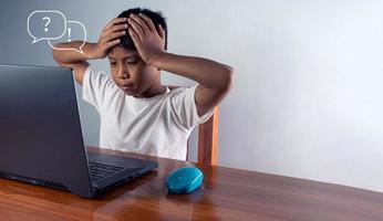 imagen del concepto de educación. idea creativa e innovación. el chico se sentó mirando la computadora y se tocó la sien. representa la incapacidad de pensar foto