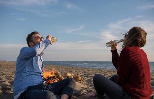 Young Couple Sitting On The Beach beside Campfire drinking beer photo