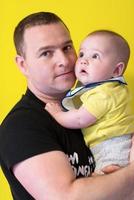 portrait of happy young father holding baby isolated on yellow photo