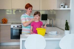 Funny little girl helper playing with dough on his hands learning to knead helps adult mom in the kitchen, happy cute baby daughter and parent mom have fun cooking cookies. photo