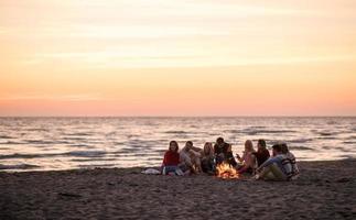 grupo de jóvenes amigos sentados junto al fuego en la playa foto