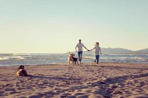 pareja con perro divirtiéndose en la playa el día del otoño foto