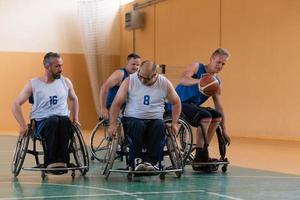 veteranos de guerra discapacitados de raza mixta que se oponen a equipos de baloncesto en sillas de ruedas fotografiados en acción mientras juegan un partido importante en una sala moderna. foto