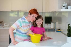 Funny little girl helper playing with dough on his hands learning to knead helps adult mom in the kitchen, happy cute baby daughter and parent mom have fun cooking cookies. photo