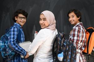 Arabic teenagers, students group portrait against black chalkboard wearing backpack and books in school.Selective focus photo