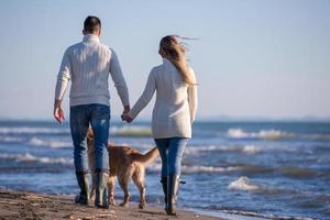 couple with dog having fun on beach on autmun day photo