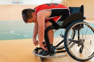 el niño se sienta en una silla de ruedas y se prepara para el comienzo del juego de baloncesto en la gran arena foto