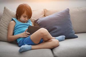 Little Arabian boy sitting on sofa and playing game on digital tablet photo