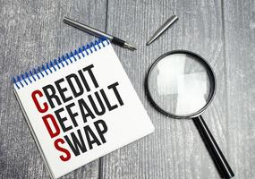 CDS Credit Default Swap text on white paper on wooden background and magnifier photo