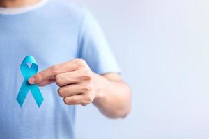 noviembre azul mes de concientización sobre el cáncer de próstata, hombre con camisa azul con la mano sosteniendo una cinta azul para apoyar la vida y la enfermedad de las personas. salud, dia internacional del hombre, padre, diabetes y dia mundial del cancer foto