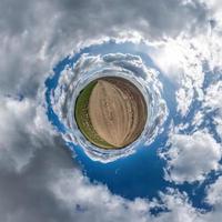 tiny planet in blue sky with beautiful clouds with transformation of spherical panorama 360 degrees. Spherical abstract aerial view. Curvature of space. photo