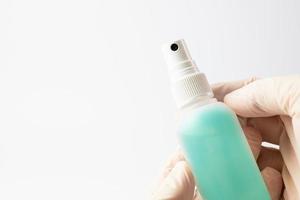 A hand in a protective glove holding a container with an antibacterial liquid on a white background. The concept of maintaining hygiene during a pandemic. photo