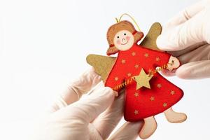 Wooden Christmas angel held in a hand in a protective glove on a white background. Christmas concept during a pandemic. photo