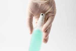 A hand in a protective glove holding a container with an antibacterial liquid on a white background. The concept of maintaining hygiene during a pandemic. photo