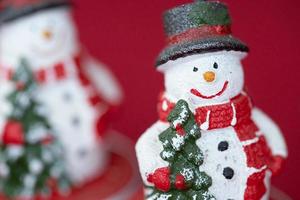 muñeco de nieve de navidad sonriente con un árbol de navidad en la mano. decoración navideña sobre un fondo rojo. foto