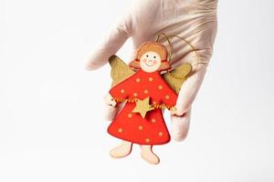 Wooden Christmas angel held in a hand in a protective glove on a white background. Christmas concept during a pandemic. photo