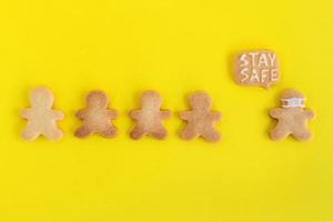 Homemade shortbread cookies with white glaze on yellow background, top view. Crowd of people and one man in face mask and with callout cloud with text - Stay safe photo