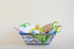 Shopping basket with baby care items - scissors, hairbrushes, pacifiers, thermometer, cotton pads and nasal aspirator - on a beige background with copy space. photo