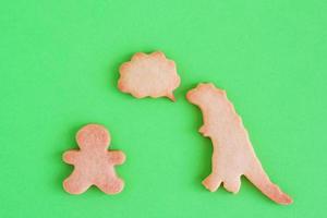 Homemade shortbread cookies in shapes of dinosaur and man with callout cloud on green background, top view. photo