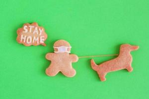 galletas de mantequilla caseras con glaseado blanco sobre fondo verde, vista superior. el hombre con mascarilla y con una llamada con inscripción - quédate en casa - está caminando con un perro. concepto de distanciamiento social. foto