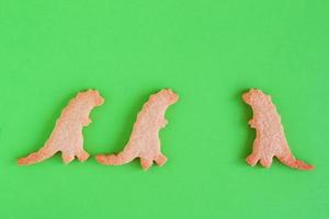 Homemade cookies in shapes of dinosaurs on green background, top view. Sweet shortbread with white glaze. Social distancing concept. photo