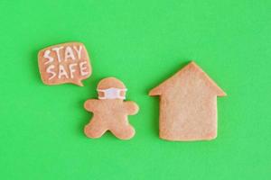 Homemade shortbread cookies with white glaze on green background, top view. Man in face mask with callout with inscription - Stay safe - near his house. Social distancing concept. photo