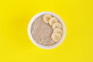 Bowl of oatmeal with banana on yellow background. Flat lay with copy space. photo