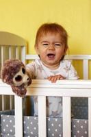 Happy one year old girl is playing with plush toy after waking up in the morning in her bed. photo