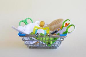 Shopping basket with baby care items - scissors, hairbrushes, pacifiers, thermometer, cotton pads and nasal aspirator - on a beige background with copy space. photo