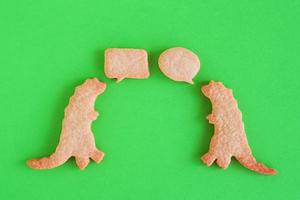 Homemade shortbread cookies in shapes of dinosaurs with callout clouds on green background, top view. photo