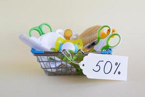 Shopping basket with baby care items - scissors, hairbrushes, pacifiers, thermometer, cotton pads, pacifier holders and nasal aspirator - on a beige background. photo